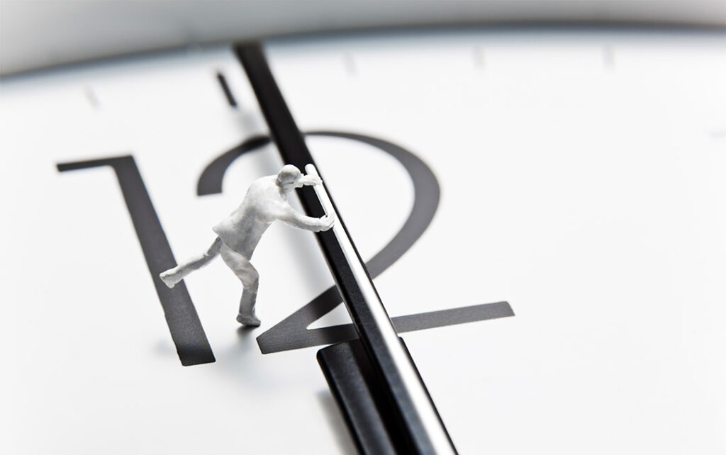 Black and white photograph of a small figurine of a man running on the face of a clock and trying to push the second hand forward.
