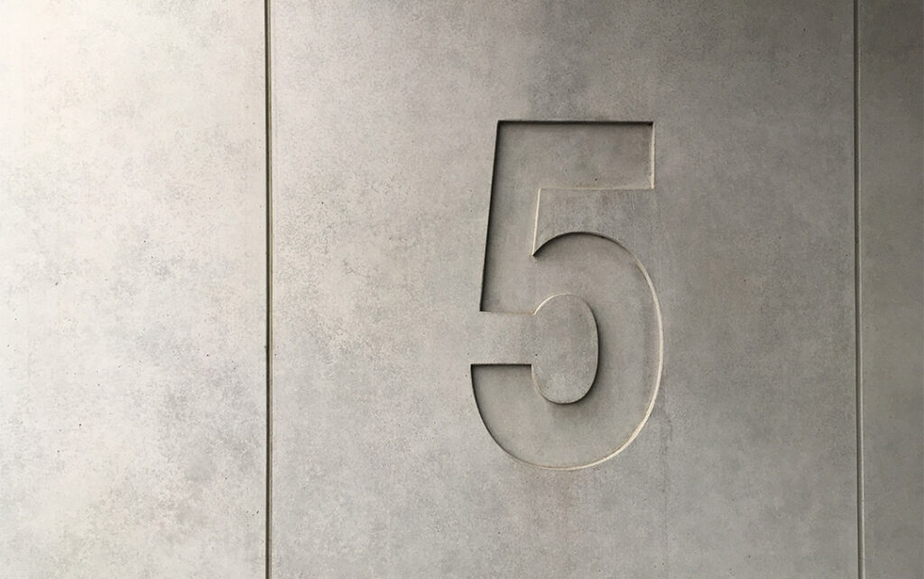 Photograph of a concrete wall with a large number "5" carved into it.