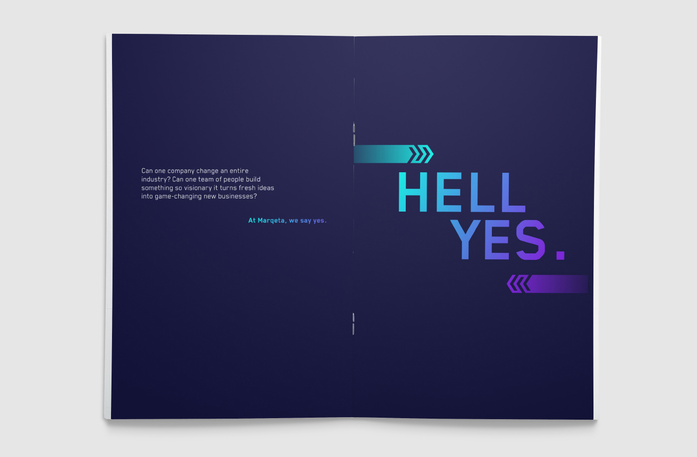 Photograph of a Marqeta booklet opened and laying flat so we see the back and front covers. They are a navy blue with a small paragraph on the left and Larger Teal, blue, to purple gradient text on the right side that reads in all capital letters " HELL YES." A teal marqeta double motion arrow is on top of the text and points to the right and a purple double motion arrow is at the bottom of the text and points to the left